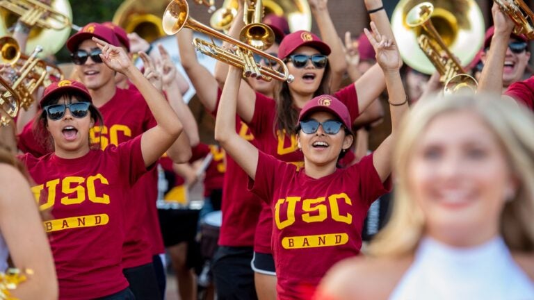 The USC band cheering during a game with the cheerleaders cheering in front of them.