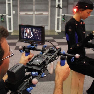 A man filming an actress that is wearing a body suit with motion sensors attached to it.
