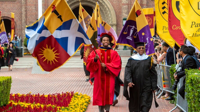 USC graduates carrying flags for their respective schools on commencement