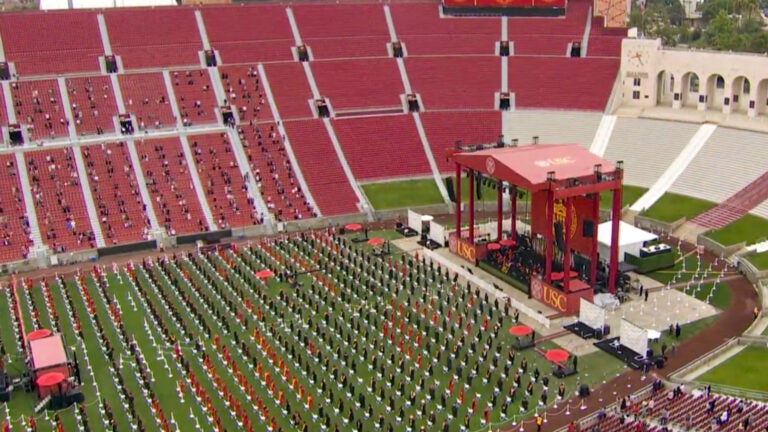A view of the coliseum from above, with a huge red stage at the center front and hundreds of grads in red gowns sitting.
