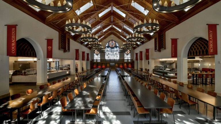 Dining hall inside USC Village, featuring long community dining tables, chandeliers, and tall ceilings with windows