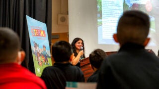 A young woman speaking in front of a podium to young students.