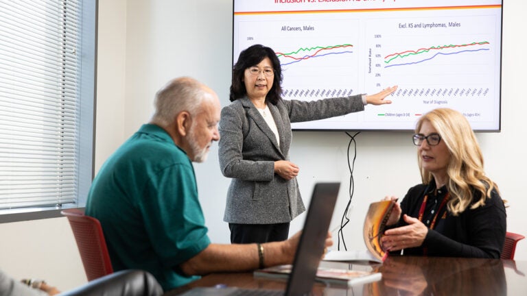 Three individuals discuss in a meeting rom looking as they look at a powerpoint