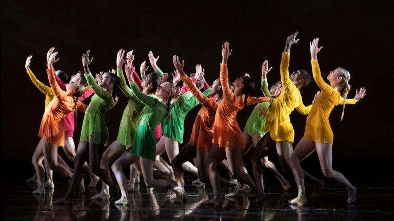 Multiple dancers in red, orange, green, and yellow dresses perform in unison.