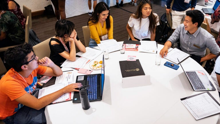 Students with laptops sit in a circle and have a conversation.