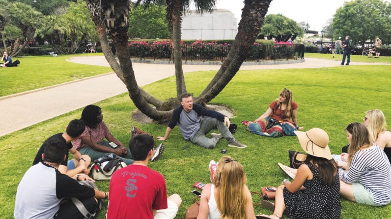 Students sit in a circle on a grass lawn on USC's campus.
