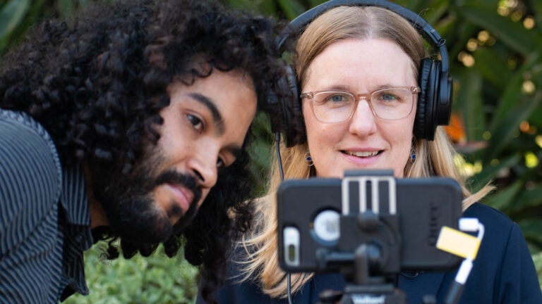 Two filmmakers look at an iphone as tehy use it to film their video.