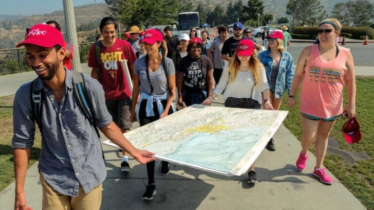 Students holding large map together as they walk down a path