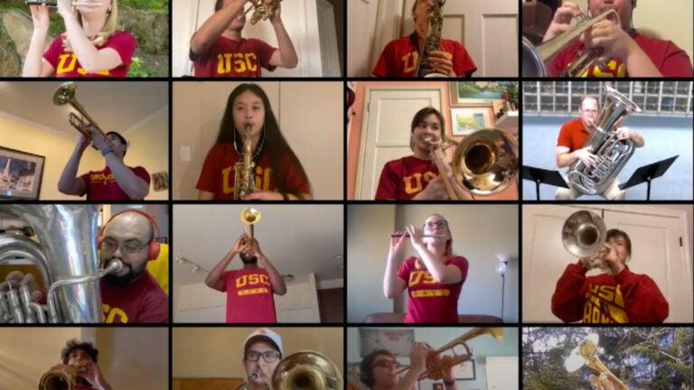 A Zoom screen with 16 marching band members in view, each play their instrument in their USC gear.