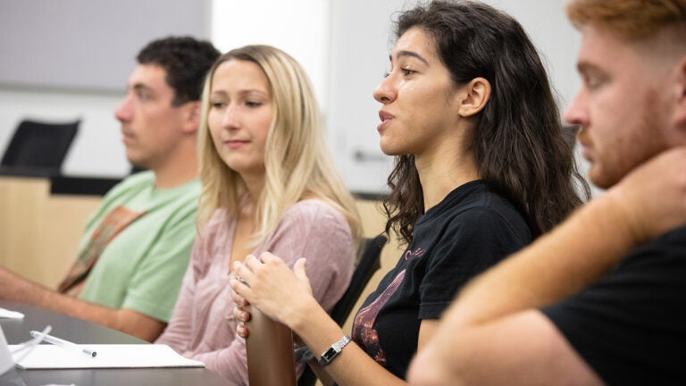 Closeup of students at a desk with the focus on one with long hair who is speaking.
