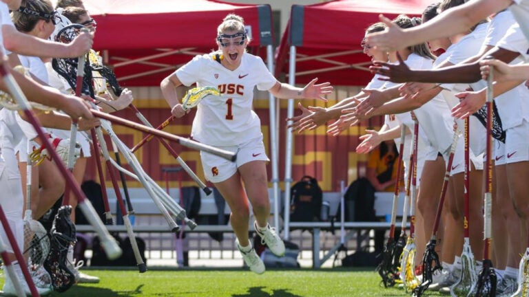 USC women's lacrosse players line up side by side as their players run through receiving high fives.