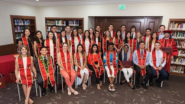 Students wearing red honors sashes pose for a group photo. They are part of the USC Sidney Harman Academy for Polymathic Study Fellows.