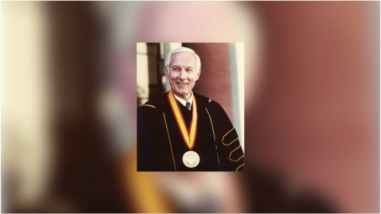 James H. Zumberge, USC's ninth president, smiling with a medal around his neck, wearing a black gown