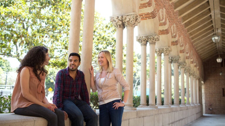 Three students take a moment to chat inside Mudd Hall with the pillars in the background