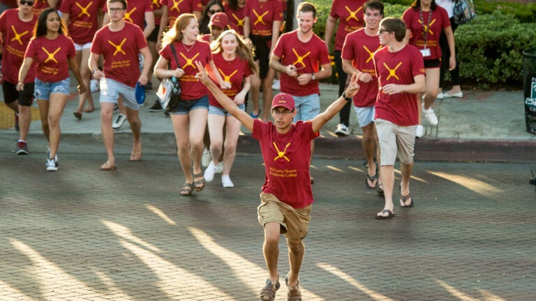Students running in a group with one man in front holding the USC hand sign.