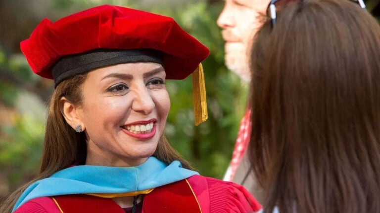 A student talking with someone in her cap and gown during commencement.