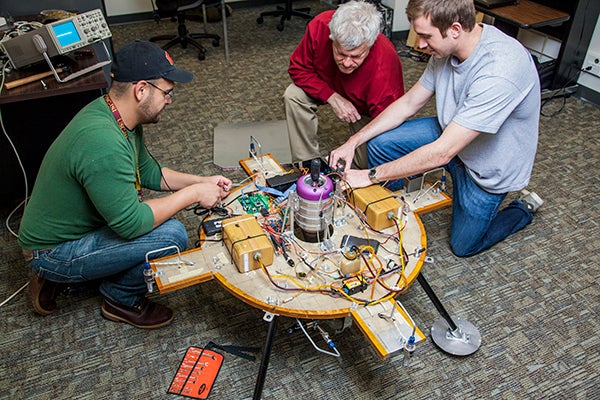 USC Viterbi School of Engineering students sitting on the floor work on an engineering project with a faculty member.