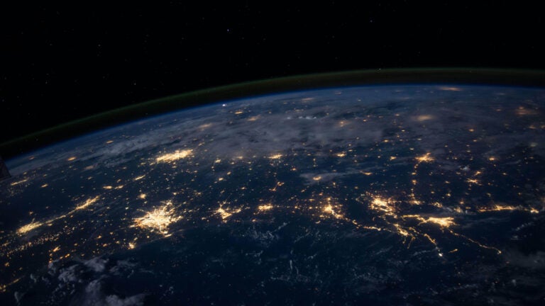 A zoomed out view of the earth from space. Lights from cities are visible.