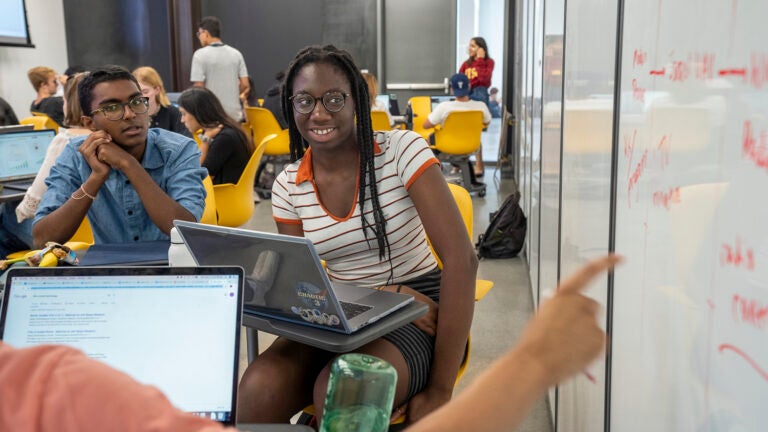 Smiling students at USC's Iovine and Young Academy sit around a white board with laptops and have a classroom discussion .