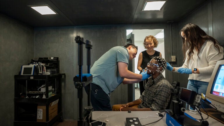 Researchers studying Alzheimer's apply brain scanning devices to a patient's head as he sits smiling in a chair.