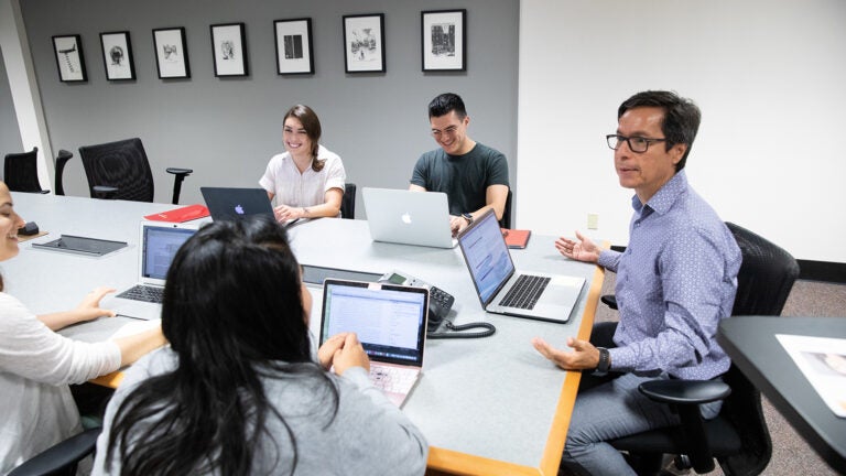 A scholar of transnationalism at the USC discusses issues of civic life at a table with students on their laptops.