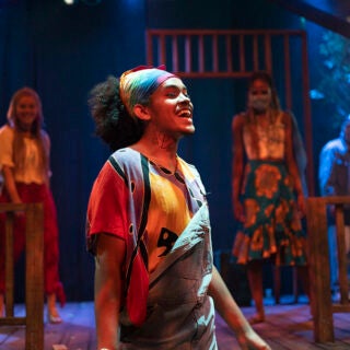 An actor singing, wearing a bandana and overalls, in a USC School of Dramatic Arts stage performance of 