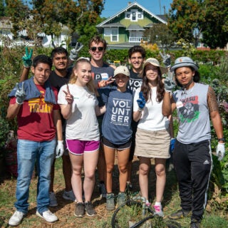 USC students pose for a group photo in a garden with gardening tools