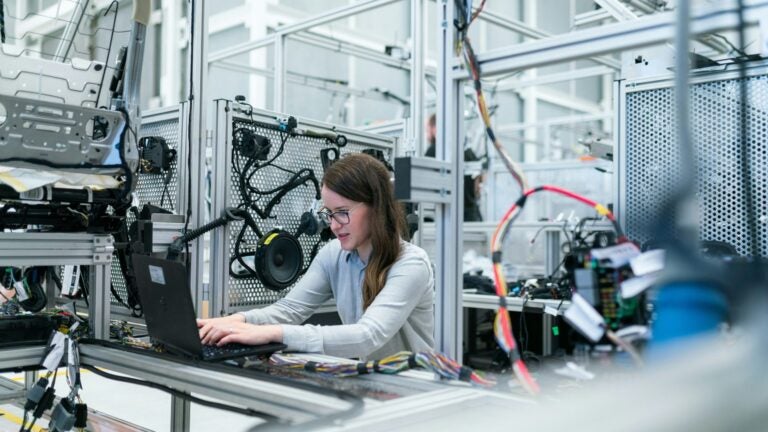 An female electrical engineer working on a computer with wiring and computer hardware surrounding her. Photo by ThisisEngineering on Unsplash