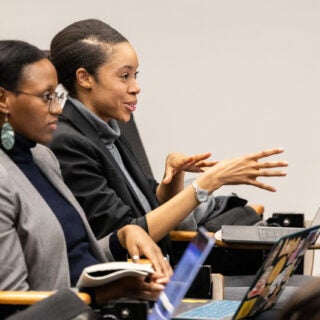 Two female students seated at a classroom responding to the speaker