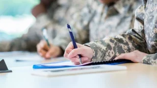 two military personnel in uniform writing on a desk