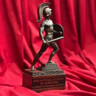Bronze Trojan statue displayed against a red fabric backdrop, commemorating the National Academy of Inventors and the University of Southern California.