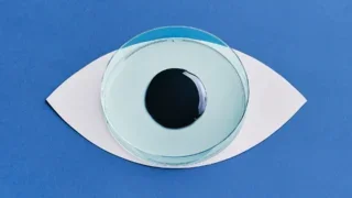 Petri dish filled with pale blue liquid and a dark circular sample, arranged to resemble an eye on a blue background.