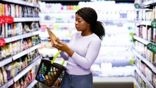 Woman reads a product label while shopping in a grocery store aisle.