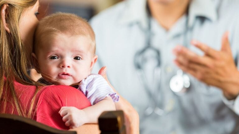 Child in mother’s arms with clinician in the background